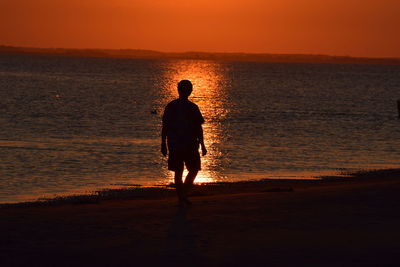 Silhouette man on beach against sky during sunset