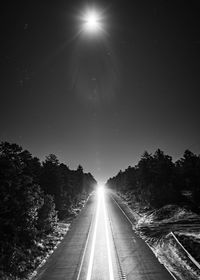 Empty road amidst trees against sky at night