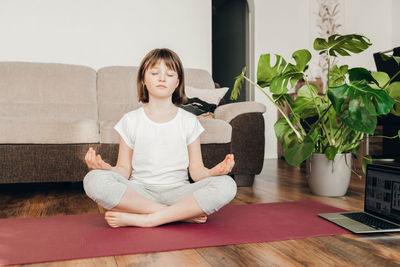 The girl sits in the lotus position and meditates at home in the living room. yoga poses for kids