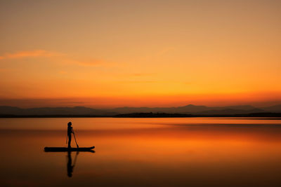 Silhouette person in lake against orange sky