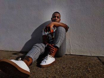 Portrait of young man sitting against wall