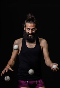 Bearded man playing with balls while standing against black background