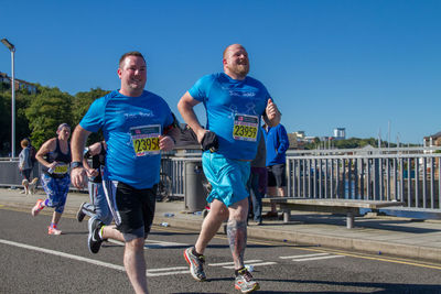 People walking on road against clear blue sky
