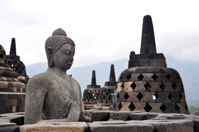 Buddha statue and stupas at borobudur against sky