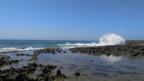 Waves splashing on shore against clear sky