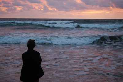 Rear view of woman looking at sea against sky during sunset