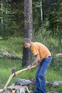 Teenage boy cutting firewood in forest