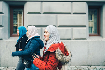 Side view of multi-ethnic female friends walking on footpath by building in city