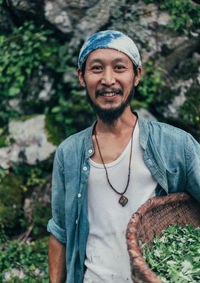 Portrait of smiling man holding basket while standing against rocks