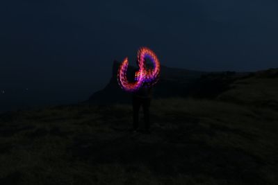Silhouette person standing on illuminated landscape against sky at night