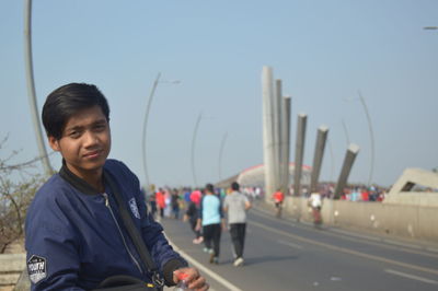 Portrait of young man standing on road against sky