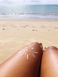 Low section of woman relaxing on sand at beach