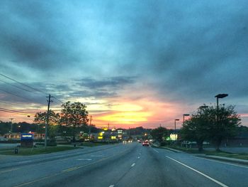 Cars on road against cloudy sky at sunset