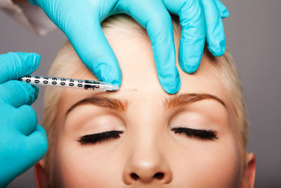 Cropped hands of surgeon giving botox injection to woman against gray background