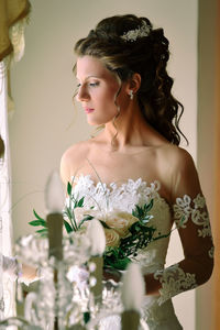 Young bride with bouquet standing at home
