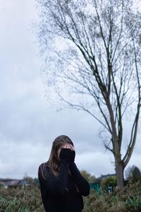 Woman covering face while standing against sky