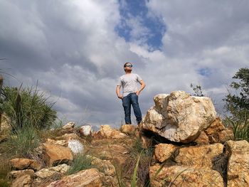 Low angle view of man standing on mountain against cloudy sky