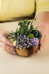 Woman holds pot with realistic exotic succulent plants of polymer clay at table