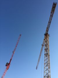 Low angle view cranes against clear blue sky