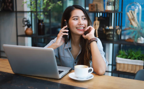 Young woman using phone while sitting on table