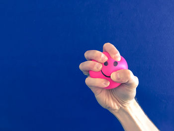 Close-up of hand holding pink flower against blue background