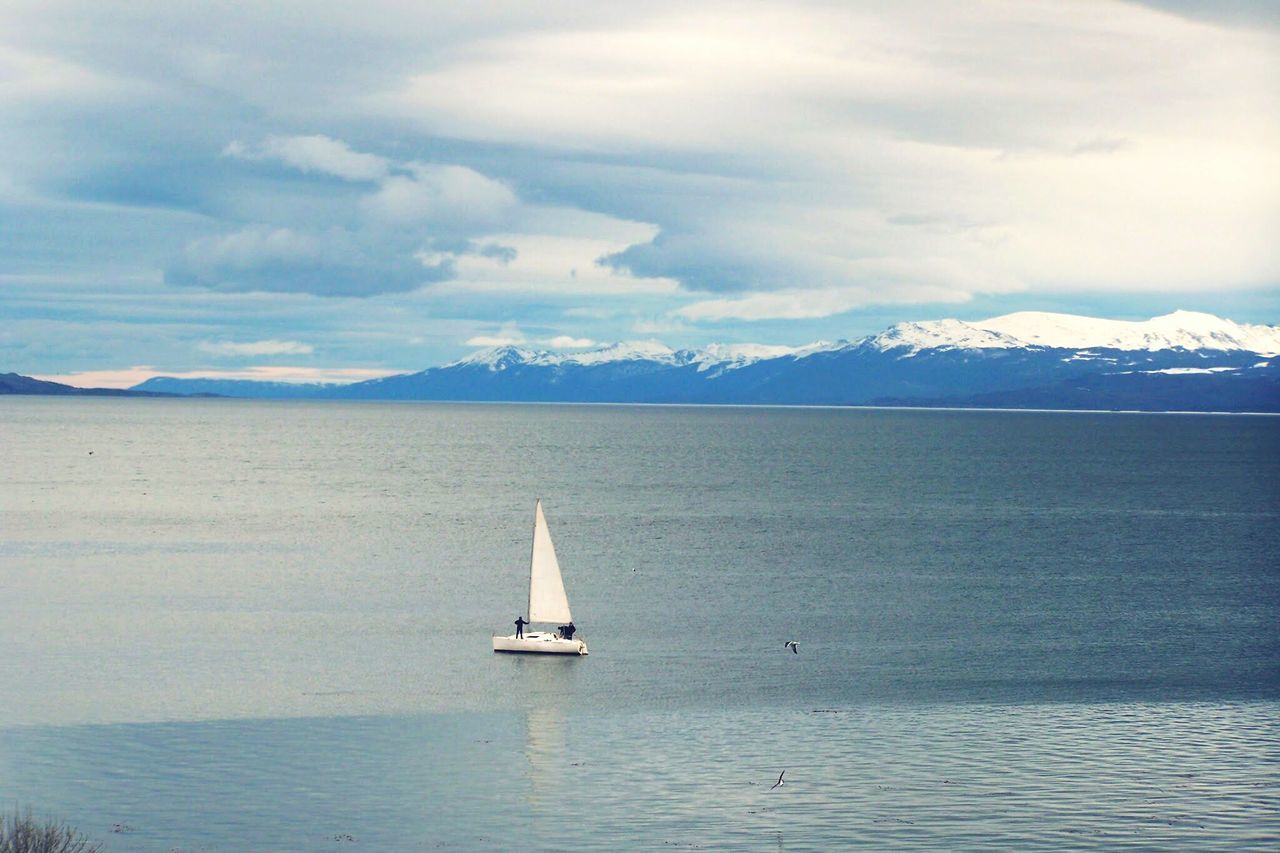 SAILBOAT SAILING ON SEA AGAINST MOUNTAIN RANGE