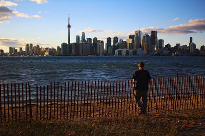 Rear view of man standing by fence at lakeshore against skyline