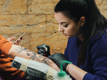 Close-up of female artist making tattoo on male customer hand