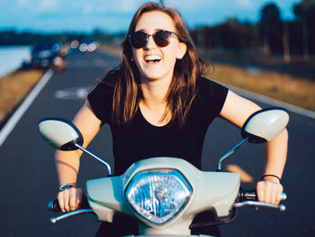 Smiling young woman sitting on motor scooter at road