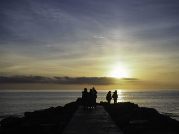 Silhouette people on pier in sea against sky during sunset