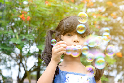Low angle portrait of cute girl blowing bubbles at park