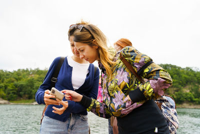 Young woman using phone while standing against sky