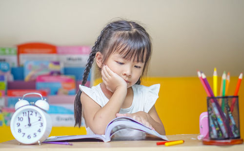 Cute girl reading book while sitting by table at home