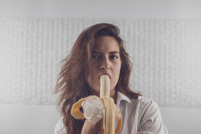 Portrait of woman eating banana against wall