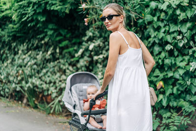 In summer pretty mother pushing a stroller with baby in the stroller.