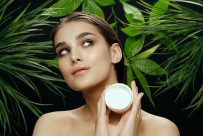 Close-up of woman holding moisturizer against plant