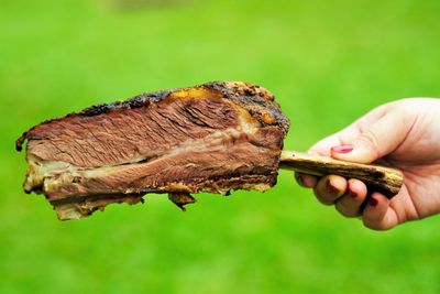 Close-up of human hand holding cooked meat outdoors