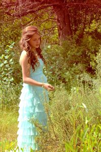 Girl in dress looking away while standing amidst plants at park