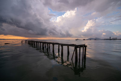 Wooden posts in sea against sky during sunset