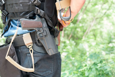 Midsection of police man with guns standing in forest