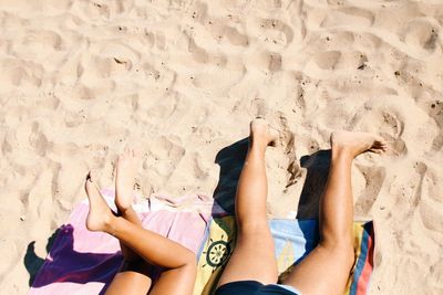 Low section of friends relaxing on sand at beach