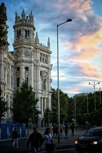 People walking on street in city against sky at sunset