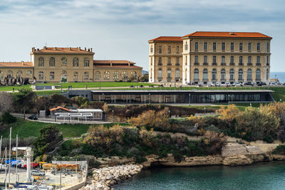 View of buildings by river in city against sky