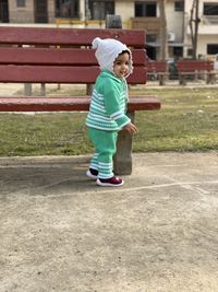 Cute baby girl standing by bench in park