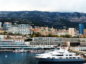 Sailboats moored on harbor by buildings against sky in city