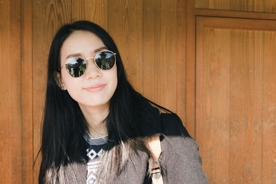 Smiling woman wearing sunglasses against wooden wall