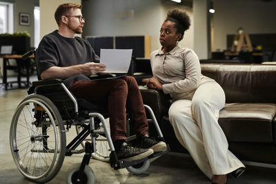 Businesswoman listening to disabled colleague on wheelchair at office