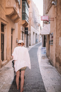 Rear view of woman walking on footpath amidst buildings