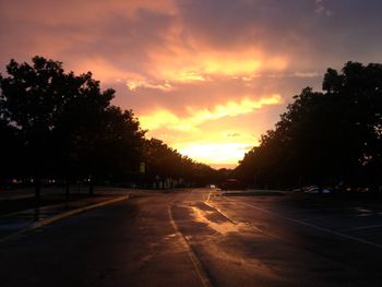 Road by silhouette trees against sky at sunset