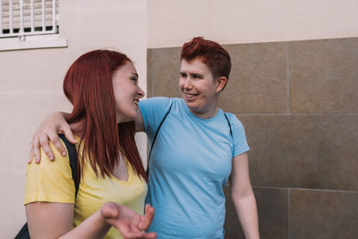 Smiling woman talking with friend walking by wall